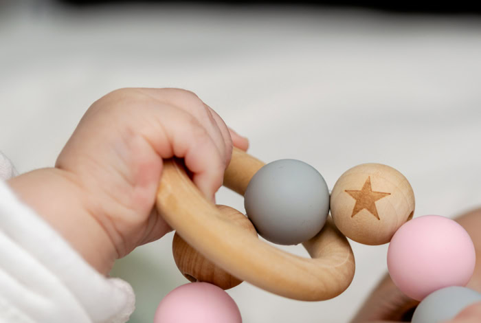 Main de bébé tenant un anneau d'éveil en bois avec des perles pastel pour développer sa motricité fine