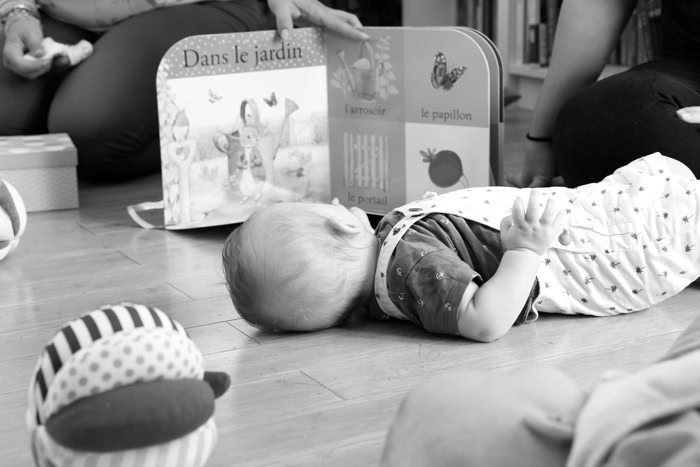 Bébé allongé sur un tapis d'éveil explorant un livre pour enfants, avec un adulte présent pour l'accompagner