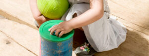 Enfant jouant avec une boîte d'encastrement en utilisant une boîte de lait recyclée pour améliorer sa motricité fine et découvrir la permanence de l'objet.