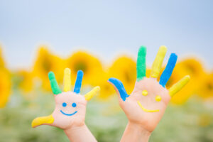 Mains d'enfant peintes avec des couleurs vives, représentant des visages souriants devant un champ de tournesols.