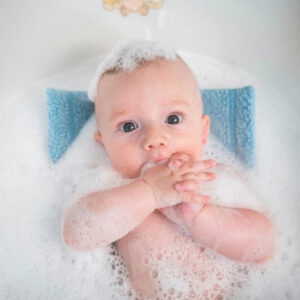 Bébé dans un bain libre, entouré de mousse, les mains jointes devant le visage