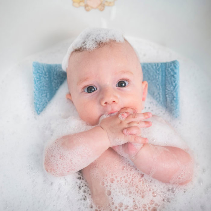 Bébé dans un bain libre, entouré de mousse, les mains jointes devant le visage