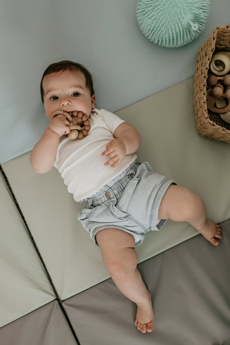 Bébé allongé sur un tapis de motricité libre, tenant un jouet de dentition en bois