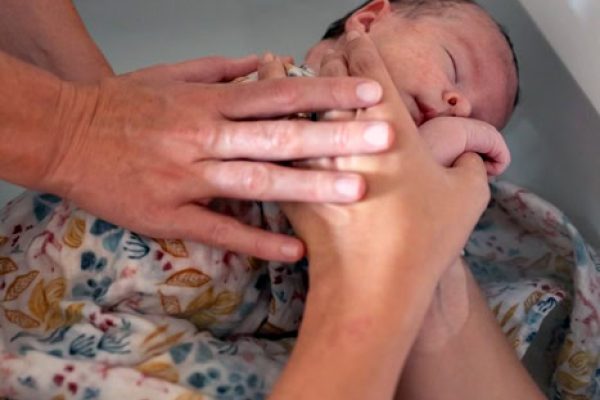 Thalasso Bain Bébé, main de parent accompagnant un nouveau-né dans un bain cocoon.